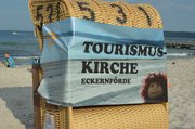 Rückansicht eines Strandkorbes mit einem Banner "Tourismuskirche"