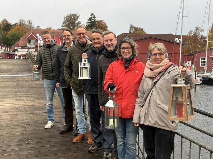 Mehrere Menschen stehen mit Laternen auf einer Holzbrücke.