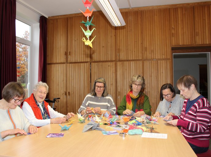 Sechs Frauen am Tisch basteln Faltkraniche.