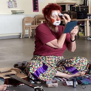 Eine Frau hat sich als Clown geschminkt. Sie sitzt auf dem Boden.