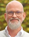 Ein Mann mit Glatze und Brille sowie eine, Vollbart.
