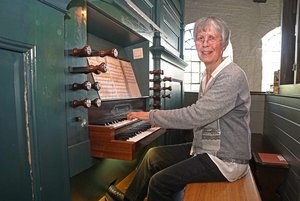 Eine ältere Frau sitzt auf einer Orgelbank und spielt am Spieltisch.
