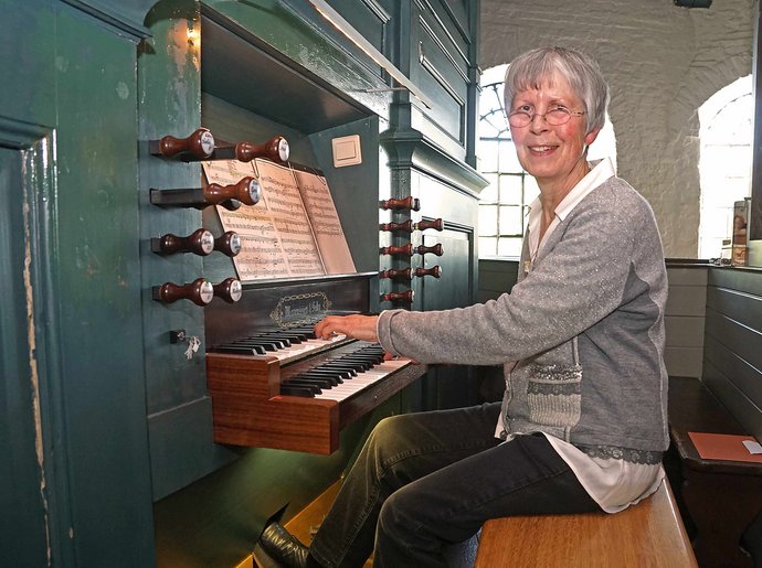 Eine ältere Frau sitzt auf einer Orgelbank und spielt am Spieltisch.