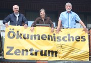 Drei Menschen halten ein Banner mit der Aufschrift "Ökumenisches Zentrum"