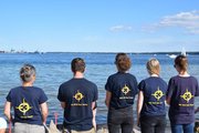 Fünf Menschen in gleichen Shirts schauen aufs Wasser