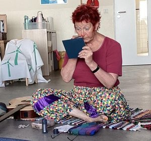Eine Frau in rotem Oberteil mit bunter Hose sitzt vor einem Spiegel und schminkt sich.