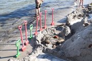 Viele Schaufeln stecken im Sand, davor Sandburgen, dahinter Wasserlinie