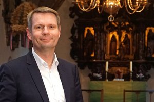 Ein Mann steht in einem Kirchraum. Im Hintergrund ist ein Altar zu erkennen.