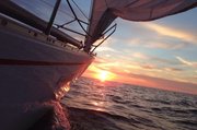 Blick auf untergehende Sonne im Meer, links die Seite eines kleinen Bootes
