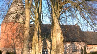Kirche in Kosel hinter kahlen Bäumen im Sonnenschein