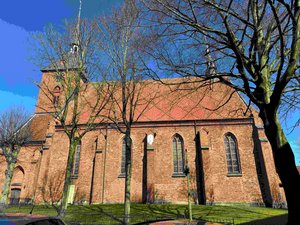 Ein Kirchgebäude im Sonnenschein als Seitenansicht, davor stehen Bäume noch ohne Laub.