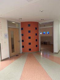 hellrosa-beige gestreifter Boden leitet über in eine Wand mit Glassteinen und dem Eingang zum Raum der Stille