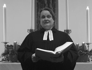 Eine Frau im Talar steht mit einem Buch vor einem Altar.