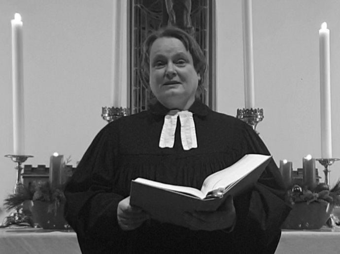 Eine Frau im Talar steht mit einem Buch vor einem Altar.