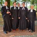 Fünf Menschen in geistlicher Kleidung stehen vor Bäumen und lächeln in die Kamera