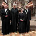 Zwei Männer und zwei Frauen, alle in schwarz, in einer Kirche