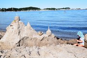 Ein Kleinkind sitzt neben einer riesigen Sandburg, im Hintergrund die Eckernförder Bucht